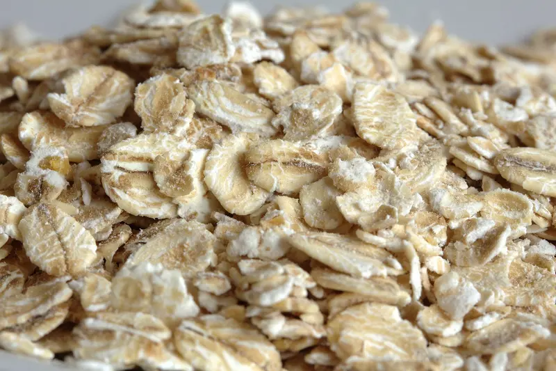 Close-up of a pile of creamy-beige rolled oat flakes with a light dusting of oat flour, the front flakes in sharp focus