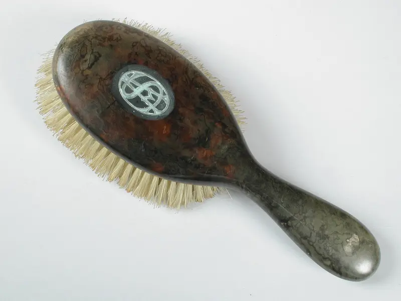 A vintage hairbrush with natural pale pig-bristle tufts and a mottled tortoiseshell back inlaid with a silver monogram, on a plain white background