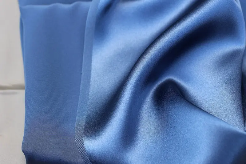 Close-up of soft folds of cornflower-blue silk charmeuse, the glossy satin face catching the light beside the duller matte reverse