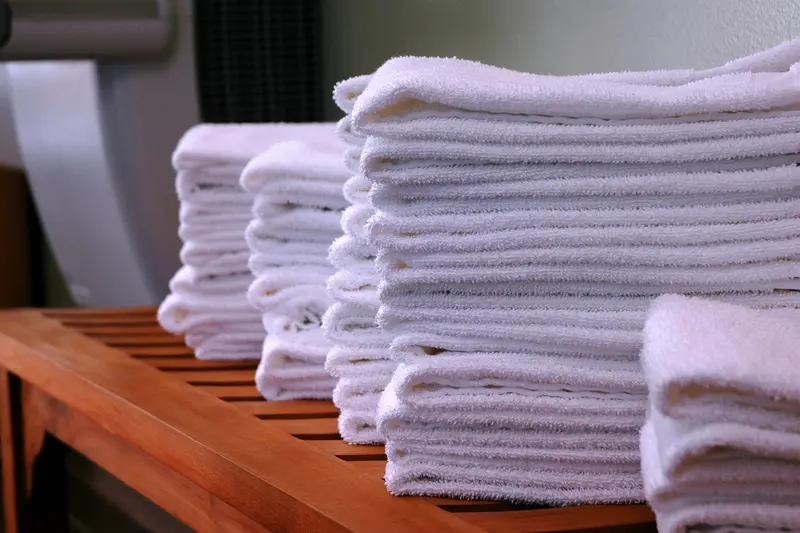 Neat stacks of folded fluffy white towels on a warm teak slatted bench, the nearest stack in sharp focus
